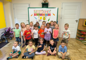 Dzieci pozują przed tablicą z napisem "Witamy"