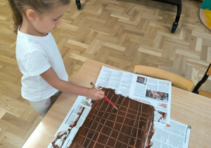 Dziewczynka "wydrapuje" linie na kartce pomalowanej farbą