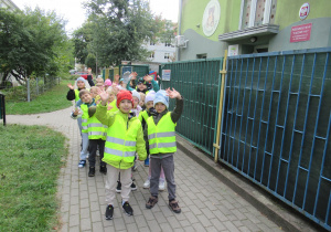 Dzieci w odblaskowych kamizelkach stoją w parach.