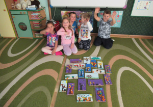 Dzieci siedzą na dywanie, przed nimi prace plastyczne - obrazki jesienne.