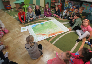 Dzieci siedzą na dywanie, przed nimi mapa Polski.