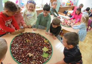 Dzieci na stolikach układają kompozycje z kasztanów i liści.