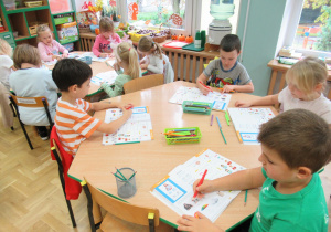 Dzieci siedzą przy stolikach i pracują w książkach.