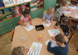 Dzieci malują farbami jesienne drzewka.