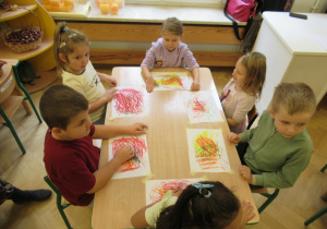 Dzieci siedzą przy stoliku i rysują.