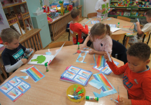 Dzieci siedzą przy stolikach i wycinają kolorowe paski.