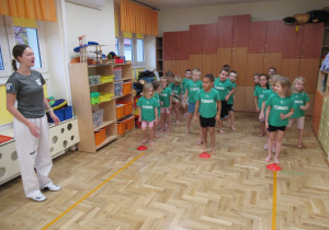 Dzieci stoją w trzech rzędach podczas zajęć z elementami teakwondo.