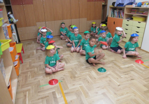 Dzieci siedzą w trzech rzędach podczas zajęć sportowych.