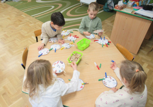 Dzieci siedzą przy stoliku i przypinają spinacze do kartoników.