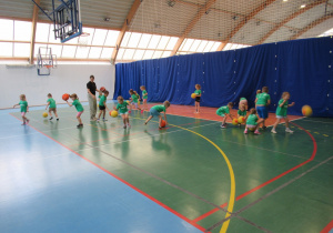 Dzieci kozłują piłki na sali gimnastycznej w szkole.