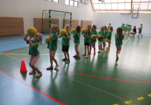 Dzieci stoją w rzędach i rzucają piłki do kosza.