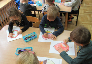 Dzieci kolorują kredkami przy stolikach.