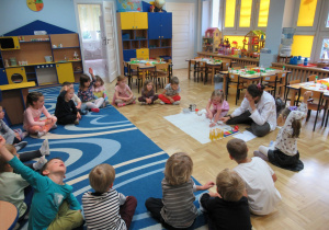 Dzieci uczestniczą w zajęciach Labo, jedna dziewcznka obok pani prowadzącej dotyka kieliszka napełnionego wodą.