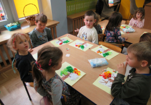 Dzieci przy stolikach wykonują prace plastyczne.
