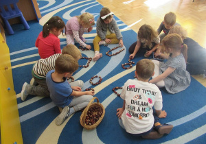 Dzieci na dywanie układają kształty z kasztanów.