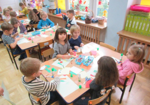 Dzieci siedzą przy stolikach i wykonują prace plastyczne.