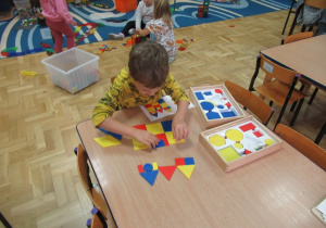 Chłopiec przy stoliku układa figury geometryczne.