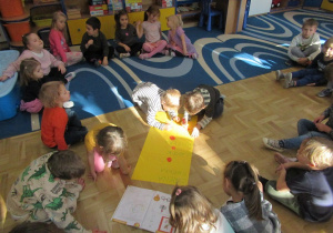 Dzieci siedzą na dywanie podczas zajęć, dwóch chłopców koloruje kółeczka na żółtej kartce.