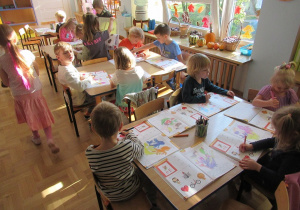 Dzieci siedzą przy stolikach i pracują w książkach.