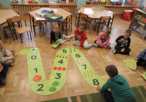 Dzieci układają na podłodze duże puzzle w kształcie węża..