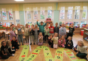 Dzieci pozują do zdjęcia, na podłodze ułożone puuzle.