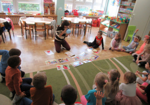Dzieci siedzą w półkolu na dywanie, przed nimi siedzi pani i nadmuchuje balon.