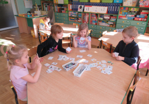 Dzieci siedzą przy stoliku i odczytują napisy na kartonikach.