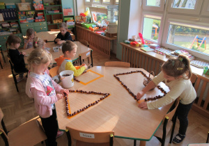 Dzieci przy stoliku układają kasztany w kształt figur geometrycznych.