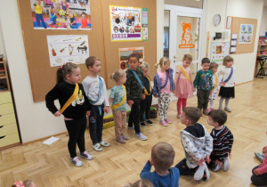 Dzieci stoją w szeregu z założonymi na siebie szarfami w kolorach żółtym i niebieskim.