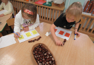 Dziewczynki siedzą przy stoliku i wykonują działania matematyczne.