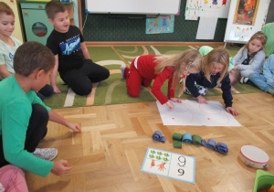 Dziewczynki wodzą palcem po napisanych na kartce cyfrach 6.