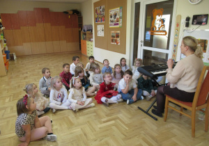 Dzieci siedzą na podłodze przed pianinem.