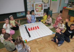 Dzieci siedzą wokół maty do kodowania, na macie ułożona flaga Polski z kubeczków.