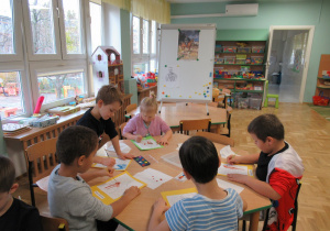 Dzieci siedzą przy stoliku i kolorują farbami wizerunek Marszałka Józefa Piłsudskiego na Kasztance.