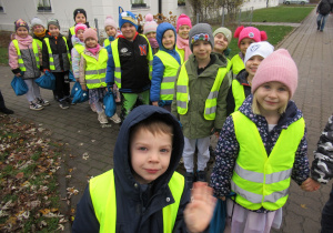 Dzieci stoją w parach w odblaskowych kamizelkach podczas spaceru.