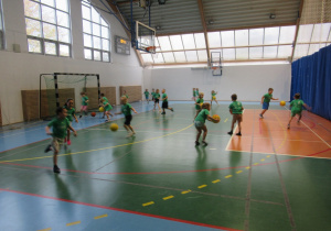 Dzieci biegają po sali gimnastycznej podczas zajęć koszykówki.