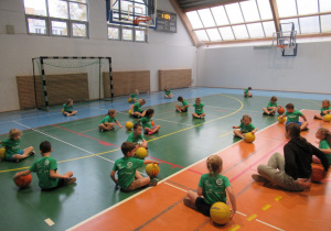 Dzieci siedzą na podłodze, toczą piłki wokół siebie.