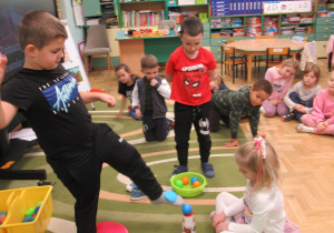 Chłopiec dotyka nogą piłeczki, inne dzieci obserwują.