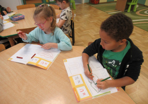 Dzieci przy stoliku i pracują w książkach.