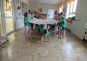 Kilkoro dzieci trzyma materiał, inne dzieci przechodzą pod nim.