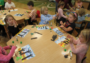 Dzieci siedzą przy stolikach i wykonują prace plastyczne.