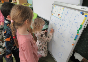 Dzieci piszą literę L na tablicy, pozostałe dzieci obserwują.