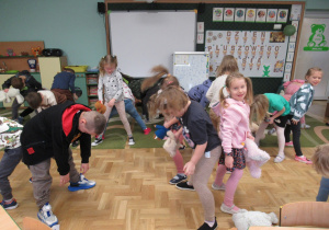 Dzieci stoją w parach plecami do siebie i podają sobie pod nogami misie.i