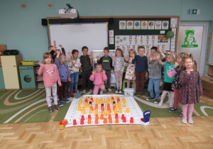 Dzieci stoją wokół maty do kodowania, na macie ułożona głowa misia z kolorowych kubeczków.