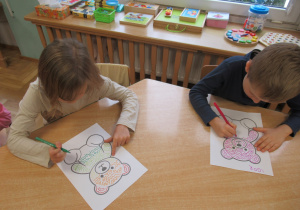 Dzieci przy stoliku wykonują karty pracy z misiem.