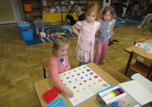 Dziewczynka siedzi przy stoliku i układa obrazki na mini macie do kodowania.