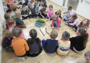 Dzieci siedzą w kole, dziewczynka kontynuuje rytm z kasztanów i orzechów.