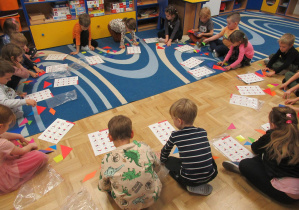 Dzieci siedzą w kole i układają tangramy.