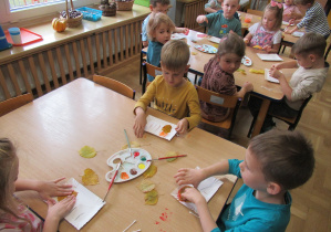 Dzieci przy stolikach wykonują prace plastyczne.