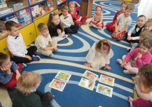 Dzieci siedzą na dywanie podczas zajęć, dziewczynka układa obrazki.